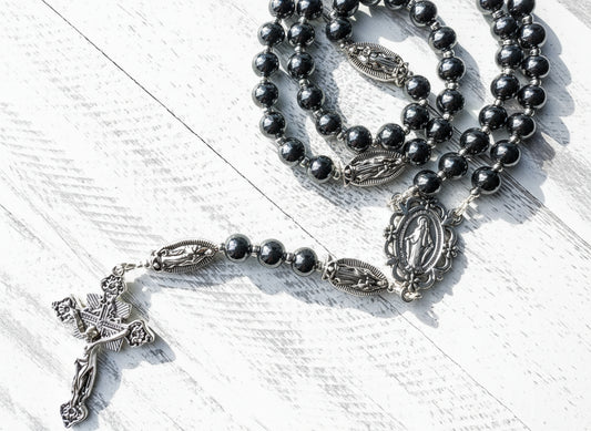 Black rosary beads with silver crucifix and our Lady of Guadalupe beads on a white wooden surface