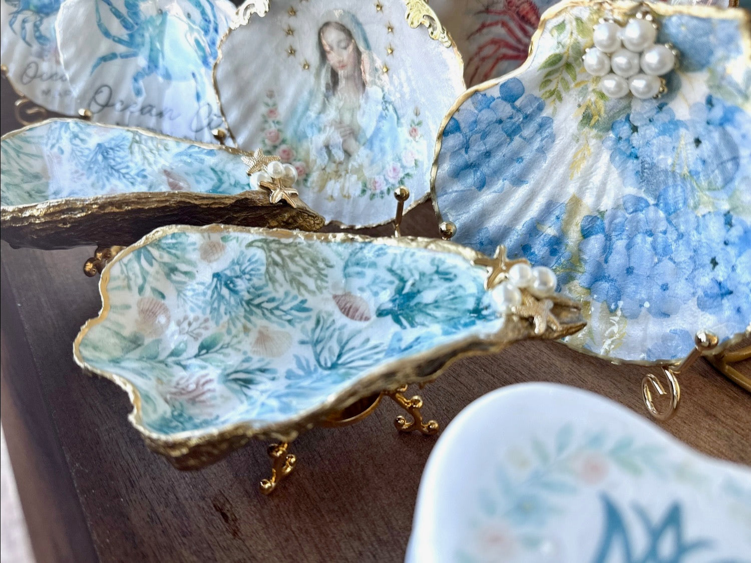 Decorative ceramic oyster shells with artistic designs and gold accents on a wooden surface.