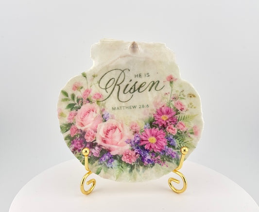 Decorative plate with floral design and 'He is Risen' text on a stand.