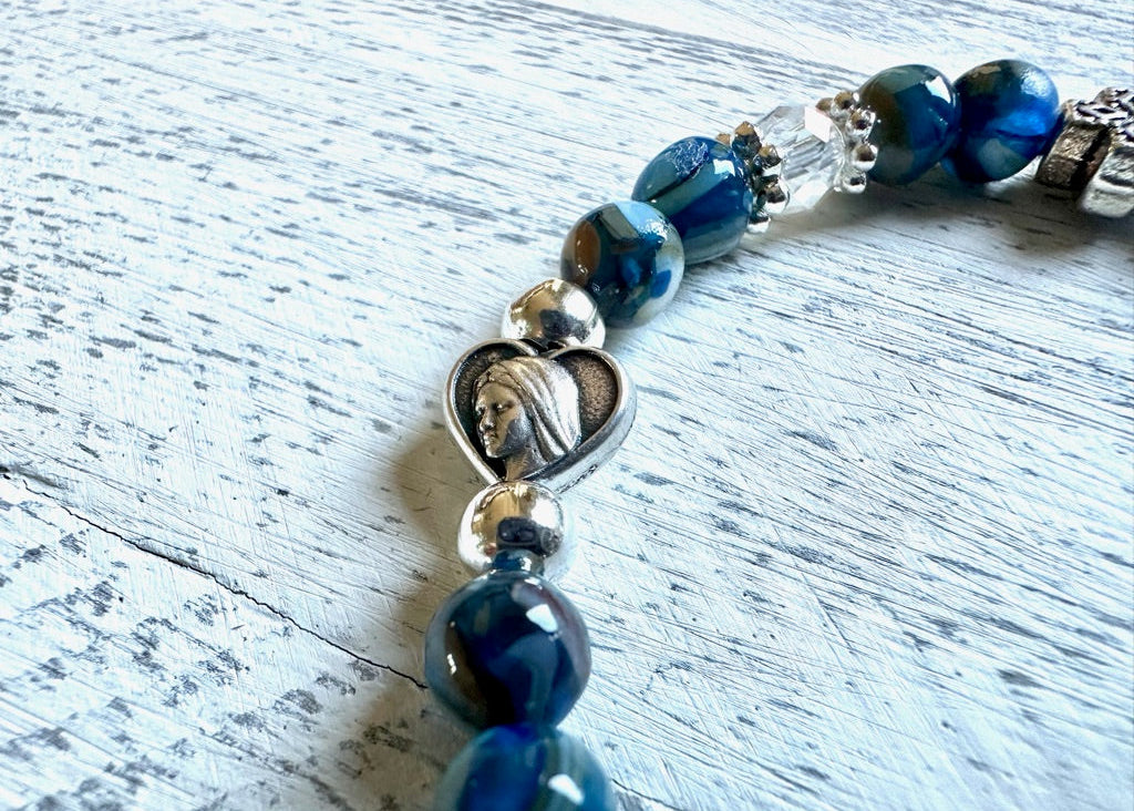 Beaded bracelet with blue beads and a silver heart charm on a light wooden surface