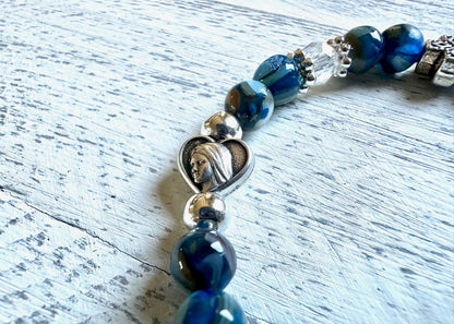 Beaded bracelet with blue beads and a silver heart charm on a light wooden surface