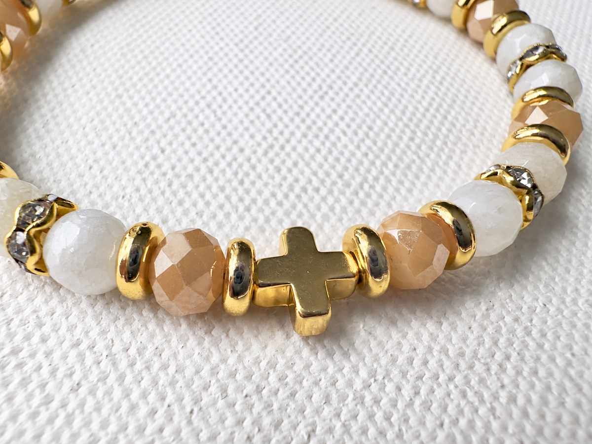 Close-up of the small gold-tone cross, 6mm champagne amber and ivory faceted glass beads and spacer details.