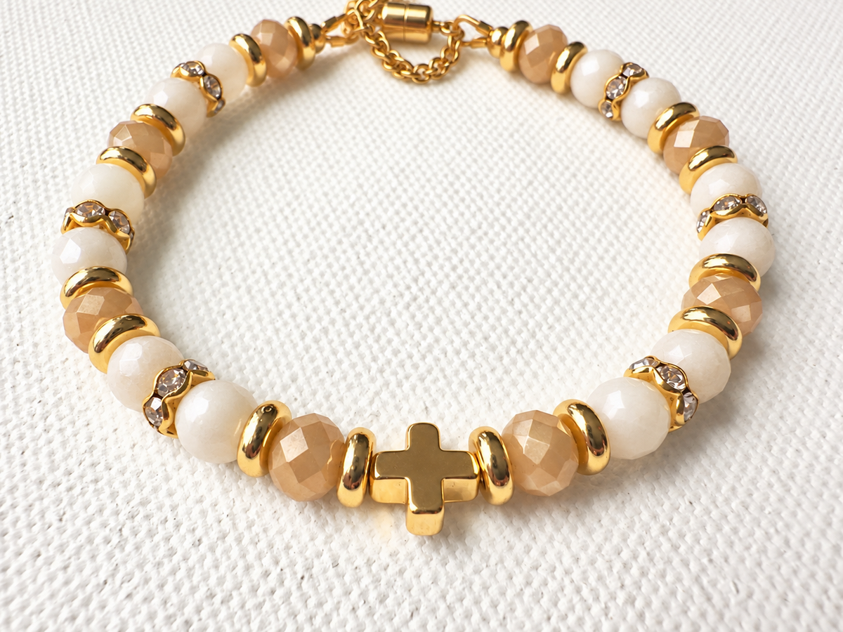 6mm faceted champagne amber and ivory glass bracelet with gold-tone cross, magnetic clasp and offset safety chain.