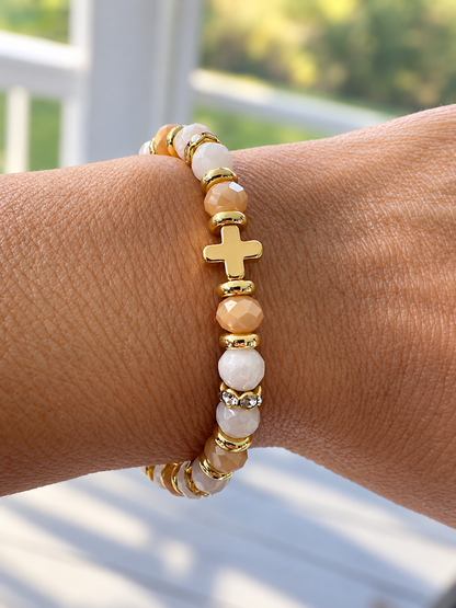 6mm champagne amber and ivory faceted glass cross bracelet worn on a woman's wrist.